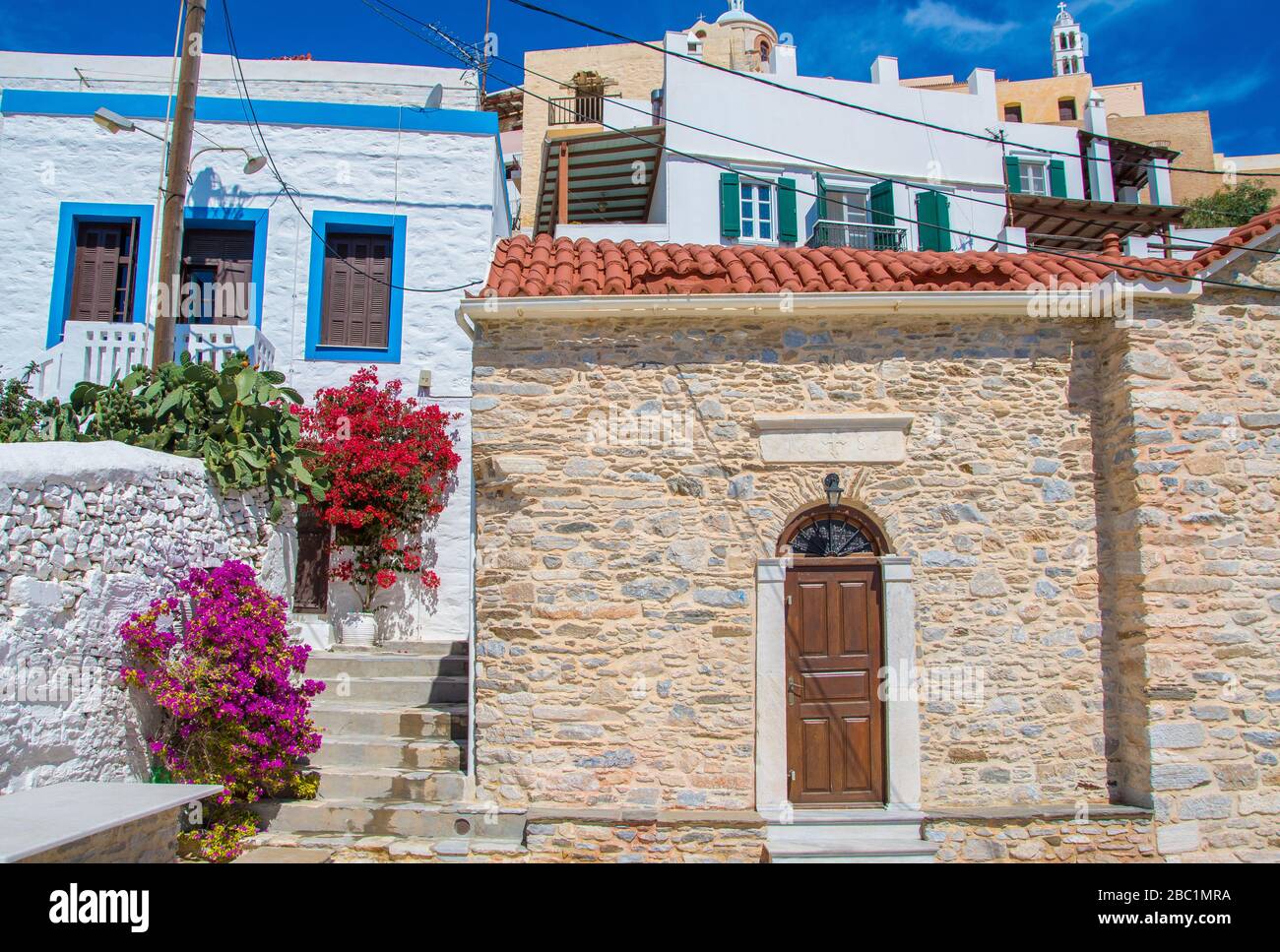 Vista sulla strada di Ano Syros con alberi di bougainvillea colorati e case tradizionali sull'isola di Syros, Grecia Foto Stock