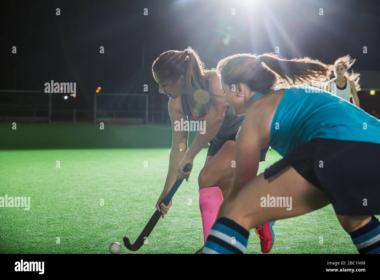 Determinate giovani giocatori di hockey da campo femminile che raggiungono il pallone, giocando sul campo di notte Foto Stock