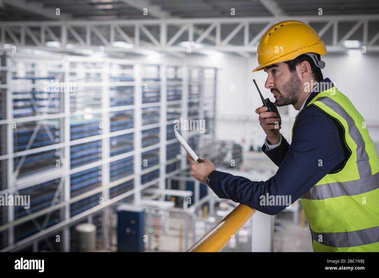 Supervisore maschile con tablet digitale che parla, utilizzando la piattaforma walkie-talkie n in fabbrica Foto Stock