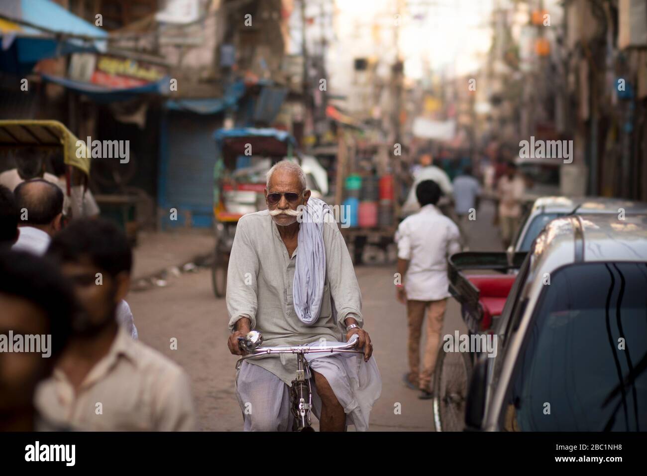 Un uomo anziano con baffi e occhiali da sole in bicicletta nella vecchia Delhi, India Foto Stock