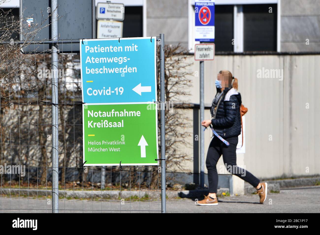Monaco, Germania. 02nd Apr, 2020. Una donna cammina con una maschera facciale, maschera protettiva dietro un segno. Troppe infezioni da corona: Muenchner Helios Klinik cede le operazioni quotidiane. A causa di un gran numero di infezioni da corona tra pazienti e dipendenti, il Muenchner Klinik cede temporaneamente le normali operazioni ospedaliere. Anche la sala d'emergenza è interessata. Le catene di infezione sono da rompere il 2nd aprile 2020 | utilizzo in tutto il mondo credito: dpa/Alamy Live News Foto Stock