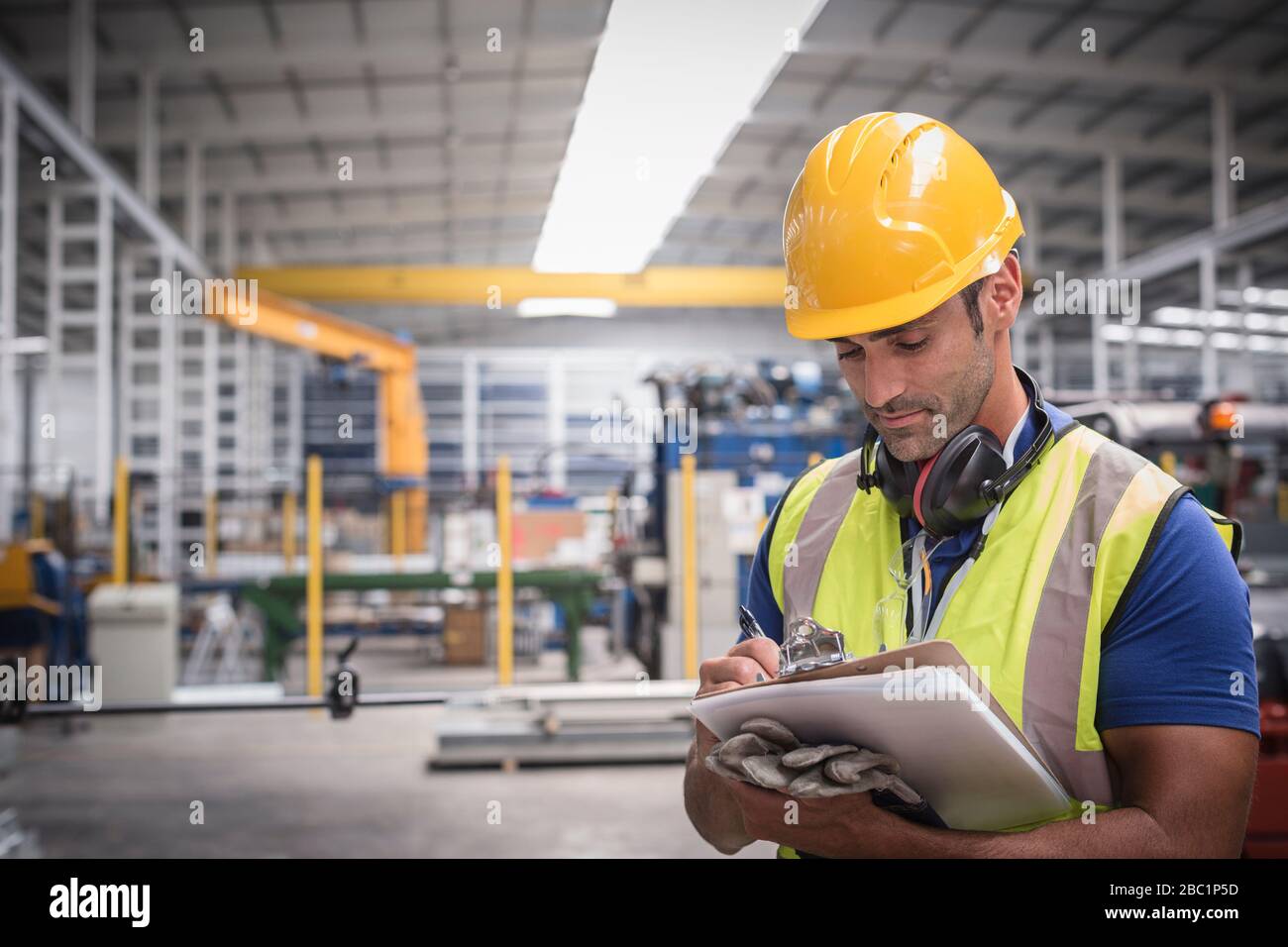 Lavoratore maschile che scrive sugli appunti in fabbrica Foto Stock