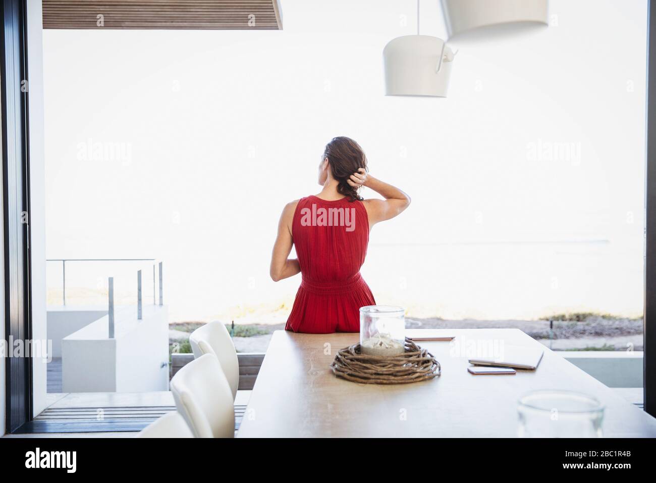 Donna brunetta con le mani in capelli che guardano fuori patio finestra Foto Stock