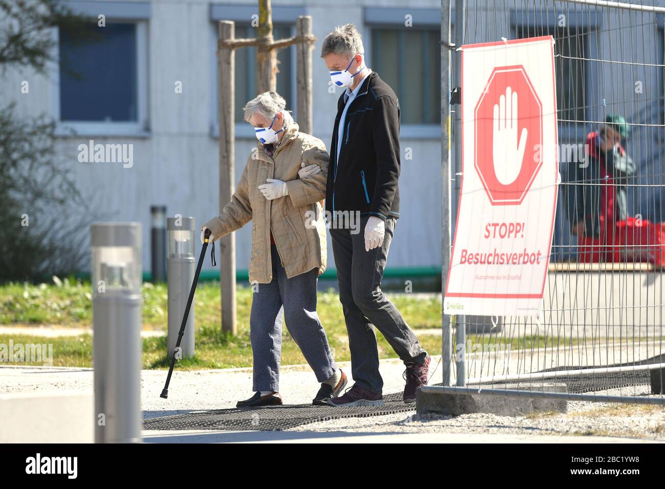 Monaco, Germania. 02nd Apr, 2020. Troppe infezioni da corona: Muenchner Helios Klinik cede le operazioni quotidiane. A causa di un gran numero di infezioni da corona tra pazienti e dipendenti, il Muenchner Klinik cede temporaneamente le normali operazioni ospedaliere. Anche la sala d'emergenza è interessata. Questo è il modo in cui le catene di infezione dovrebbero essere rotte. Un uomo più anziano e una donna più anziana escono dall'ospedale con maschere protettive, maschere facciali e guanti protettivi oltre un segno STOP! BESUCHSV Amburgo HamburgERBOT il 2nd aprile 2020. | utilizzo credito mondiale: dpa/Alamy Live News Foto Stock
