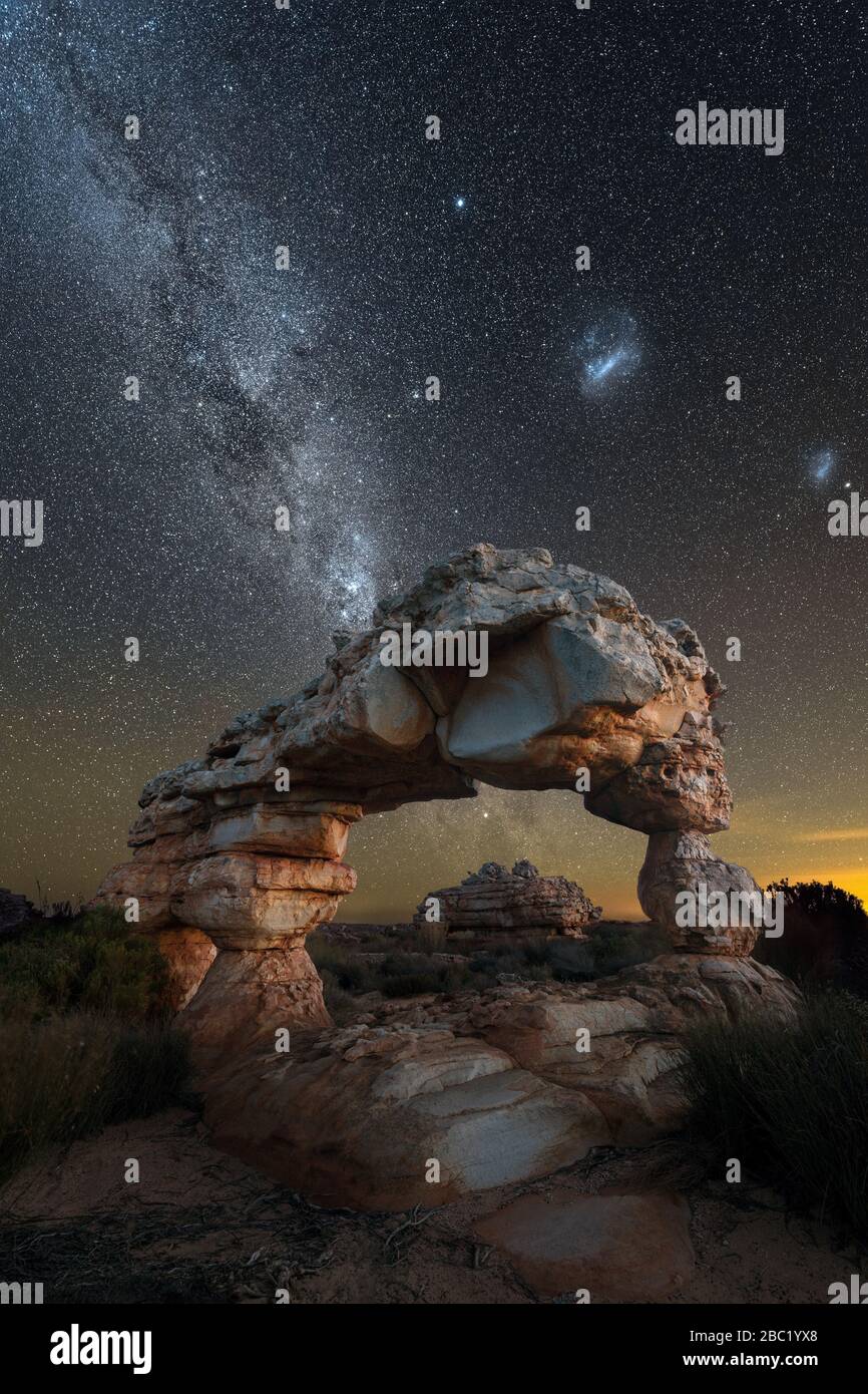 Una spettacolare fotografia verticale di un paesaggio notturno di un incredibile arco di roccia, con la Via Lattea e le nuvole Magellaniche sullo sfondo, preso in th Foto Stock