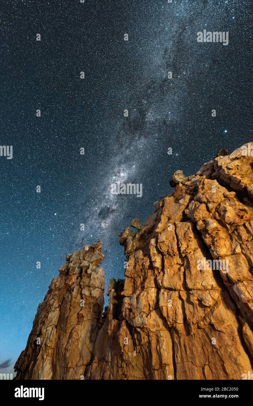 Un bellissimo paesaggio verticale di cielo notturno, con una formazione di roccia gialla in primo piano e la Via Lattea contro un cielo blu profondo sullo sfondo, Foto Stock