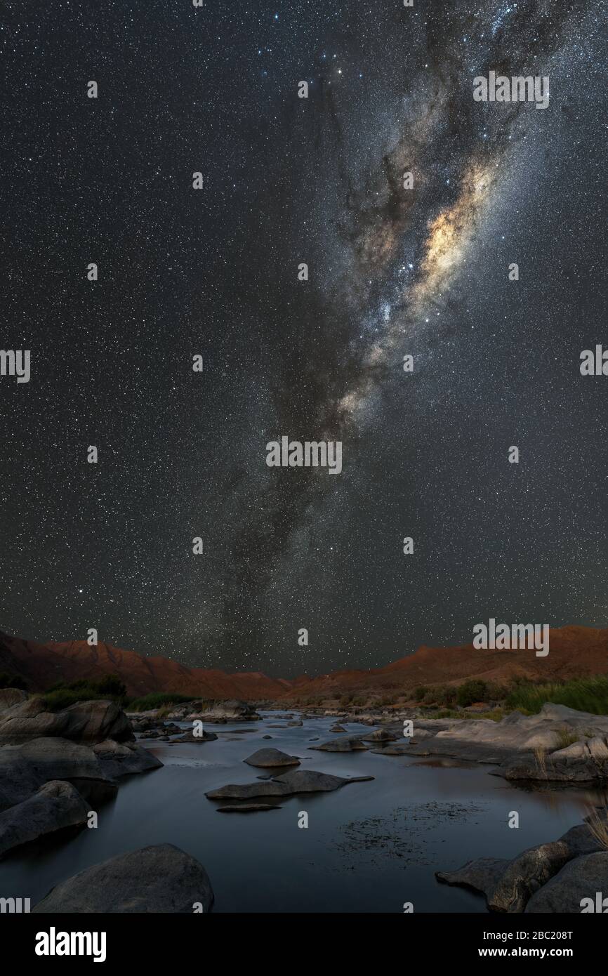 Un bellissimo paesaggio verticale notturno con la Via Lattea e il centro galattico, e il fiume Orange in primo piano e le montagne all'orizzonte, Foto Stock