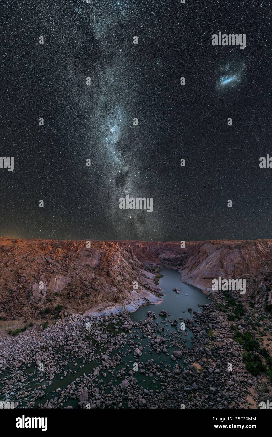 Una maestosa fotografia verticale del cielo notturno con la Via Lattea e le Nuvole Magellaniche nel cielo blu profondo, con vista sul fiume e le montagne alla A Foto Stock