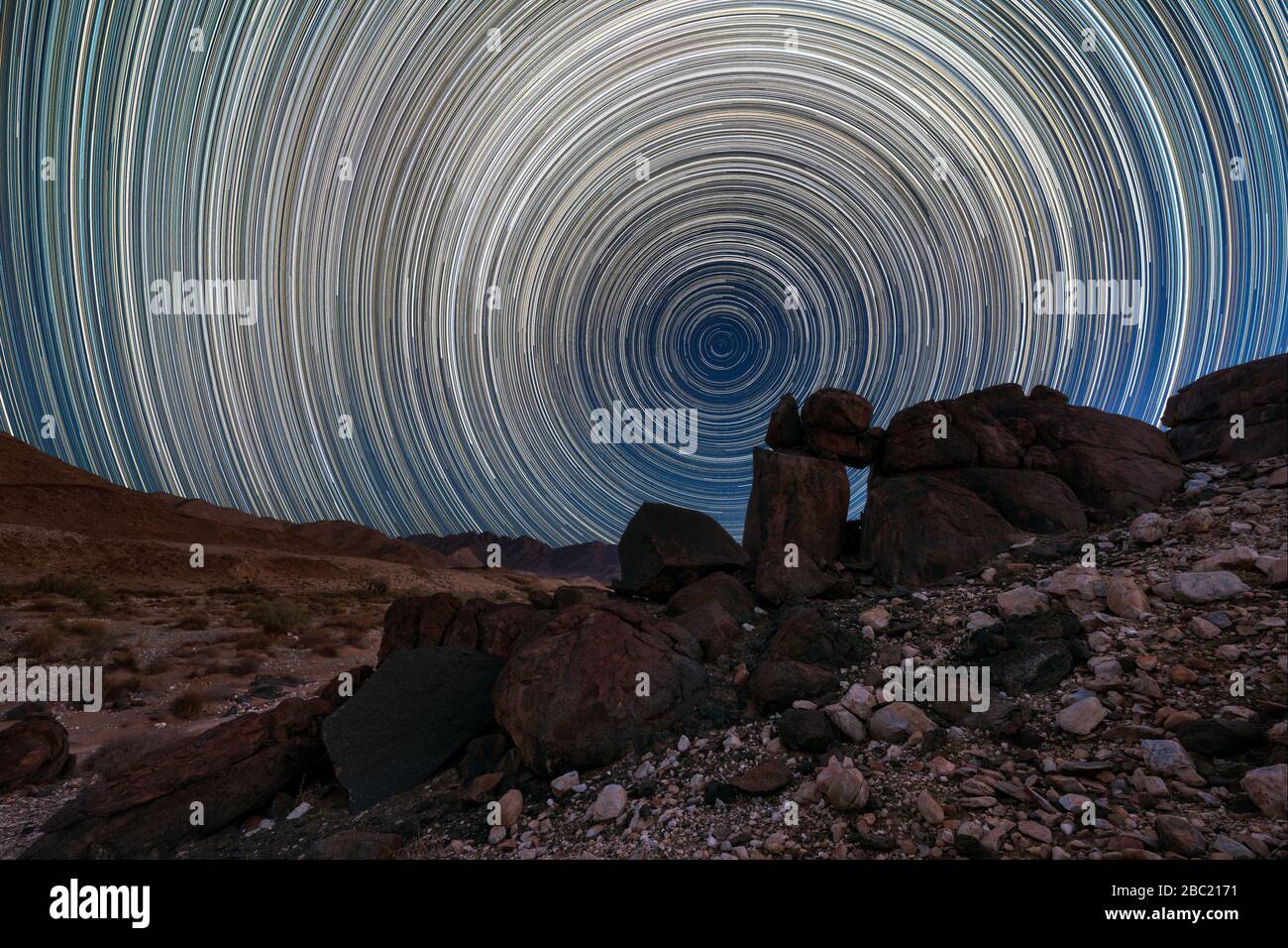 Un bellissimo paesaggio notturno con percorsi circolari stellari e interessanti formazioni rocciose in primo piano e montagne all'orizzonte, nei ricchi Foto Stock