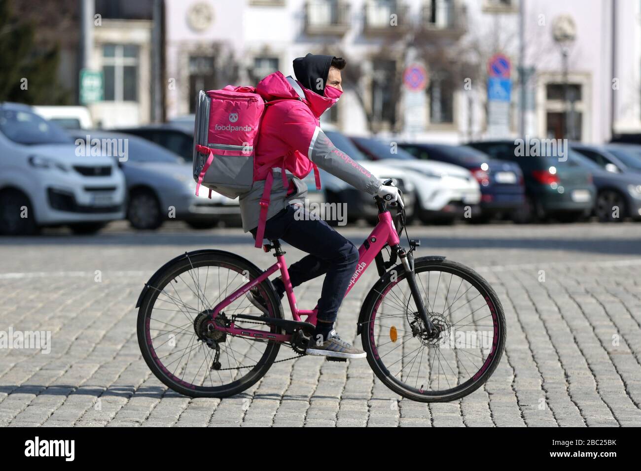 Sofia, Bulgaria - 30 marzo, 2020: Un lavoratore di Foodpanda, azienda di distribuzione online di prodotti alimentari, guida una bicicletta con cibo a un indirizzo. Indossare un dispositivo di protezione Foto Stock