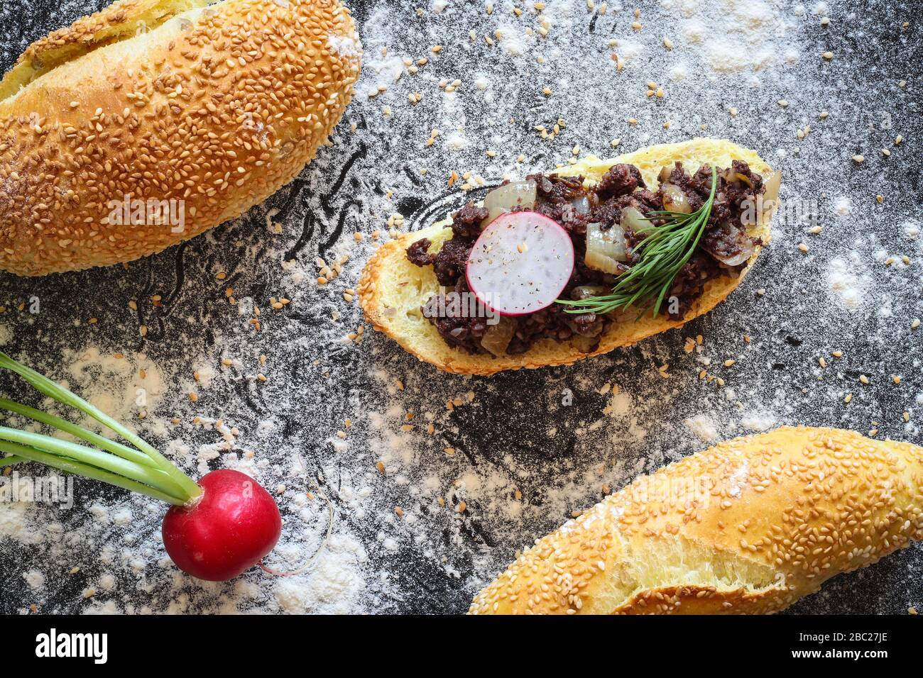 Rotolo di pane di mais con kaszanka caldo (salsiccia di sangue lucidato) stufato con cipolla su sfondo nero cosparso di farina Foto Stock