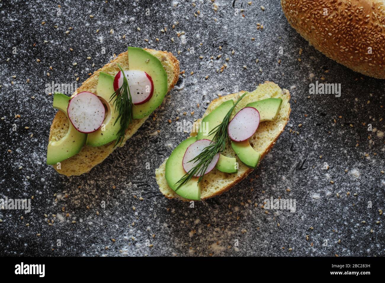 Panini vegani fatti di rotolo di pane di mais con avocado, ravanello e aneto su sfondo nero cosparso di farina Foto Stock