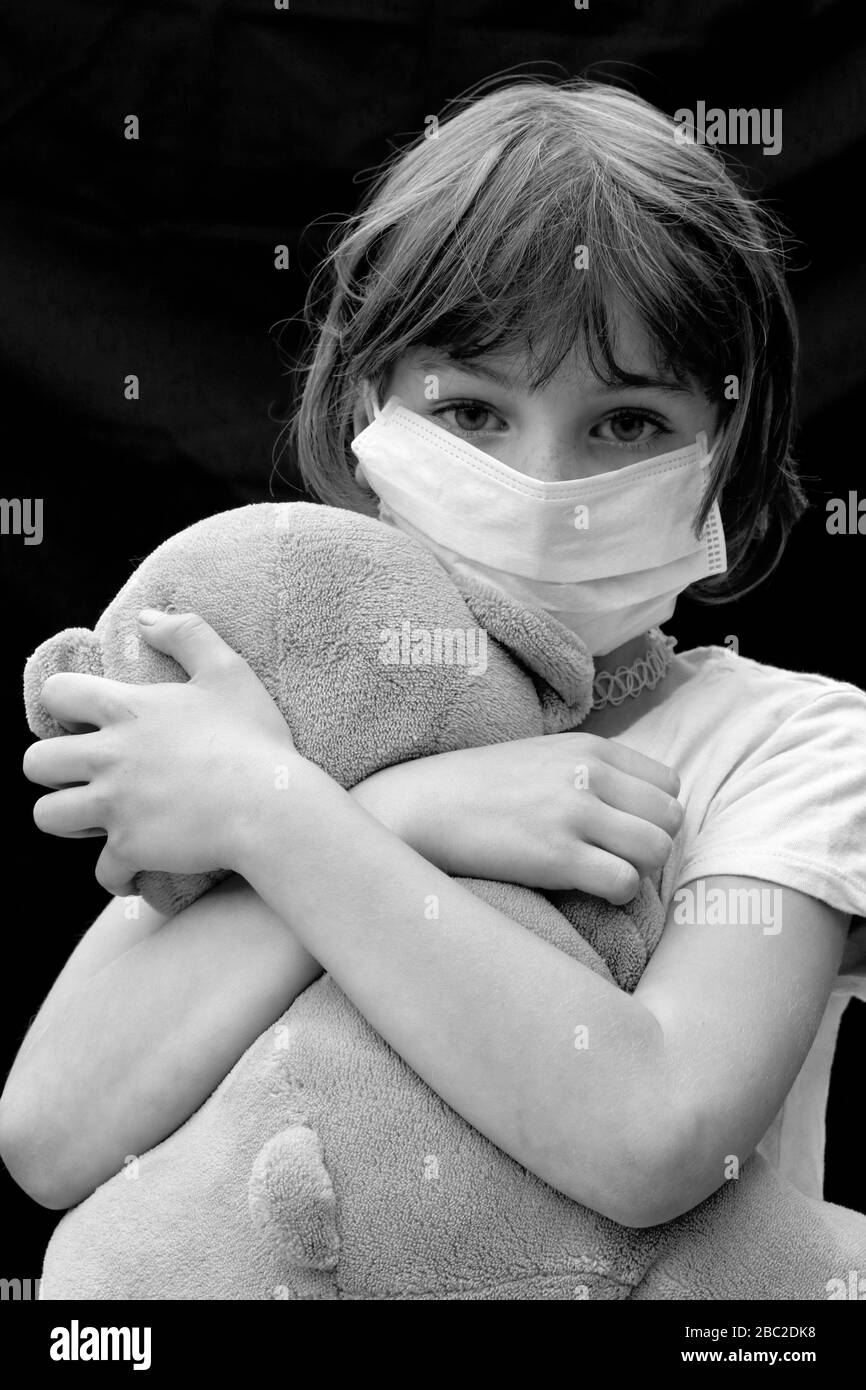 Ritratto in bianco e nero di un bambino giovane che indossa la maschera del viso con un orsacchiotto Foto Stock