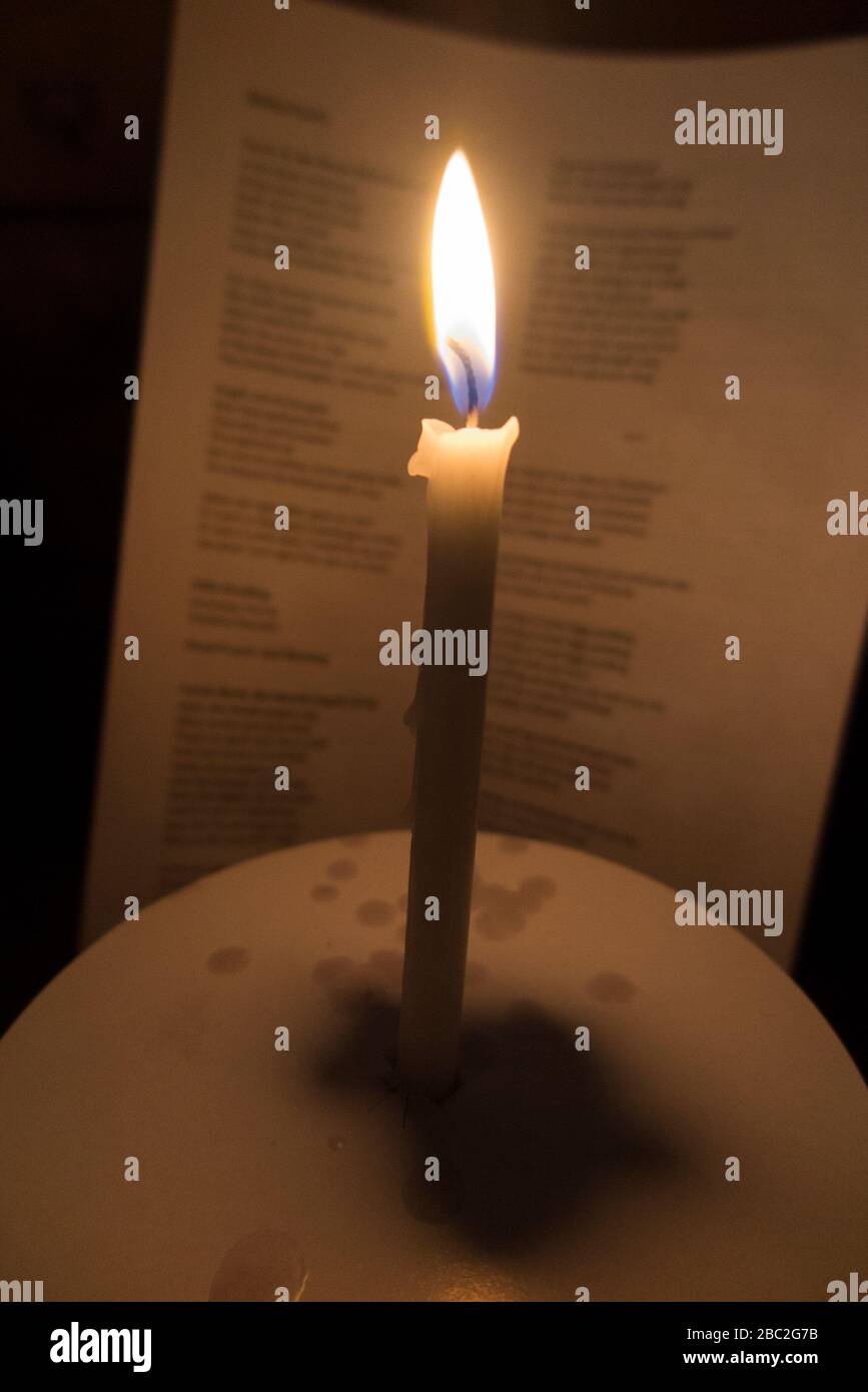 Candela della chiesa con una fiamma ardente fotografata durante un concerto di servizio di natale carol a Natale. Le parole dei caroli sono visibili sul foglio di inno dietro. Inghilterra (116) Foto Stock