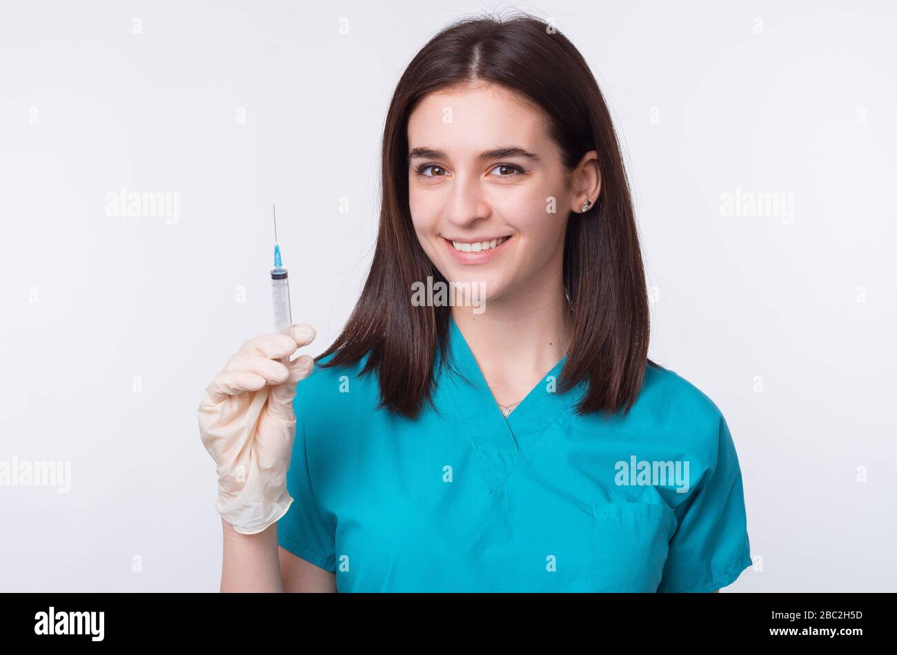Una foto di un giovane medico femminile sta tenendo una siringa, sorridendo alla fotocamera su sfondo bianco. Foto Stock