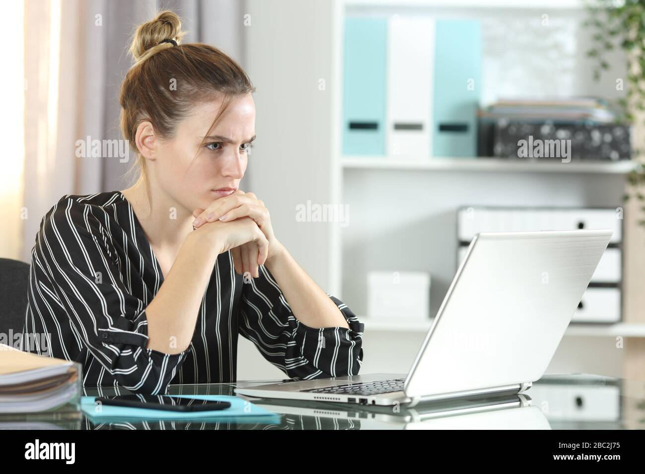 Donna imprenditrice confusa che guarda il portatile seduto su una scrivania in ufficio Foto Stock