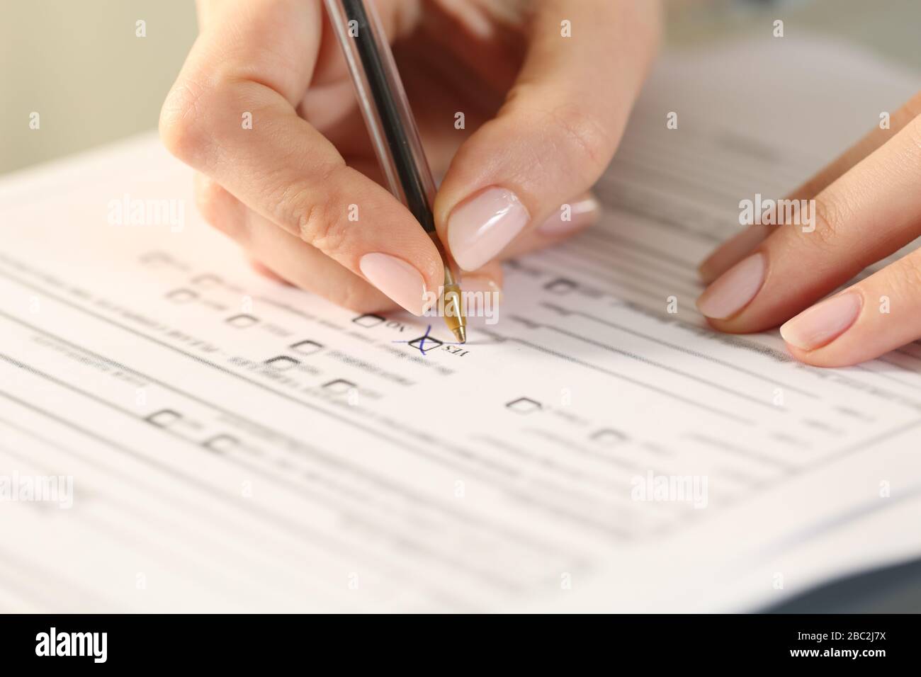 Primo piano di mani donna compilazione modulo attraversamento si casella di controllo su una scrivania Foto Stock