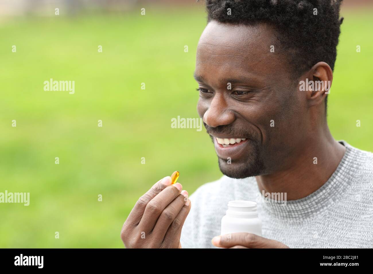 Ritratto di un uomo nero felice prendendo la pillola di vitamina omega3 nel parco Foto Stock