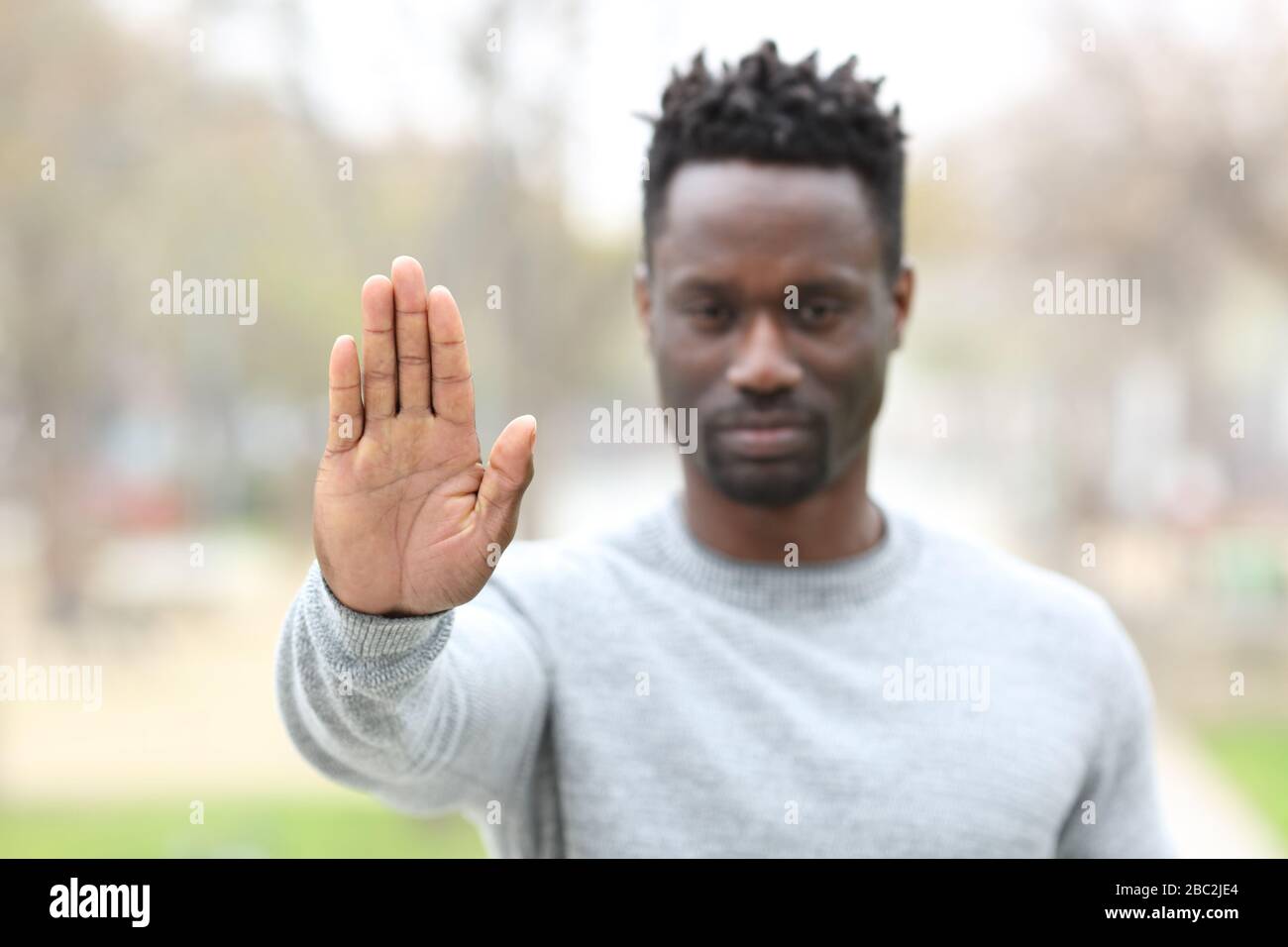Vista frontale ritratto di un uomo nero arrabbiato che gesture stop mostrando mano palma all'aperto in un parco Foto Stock