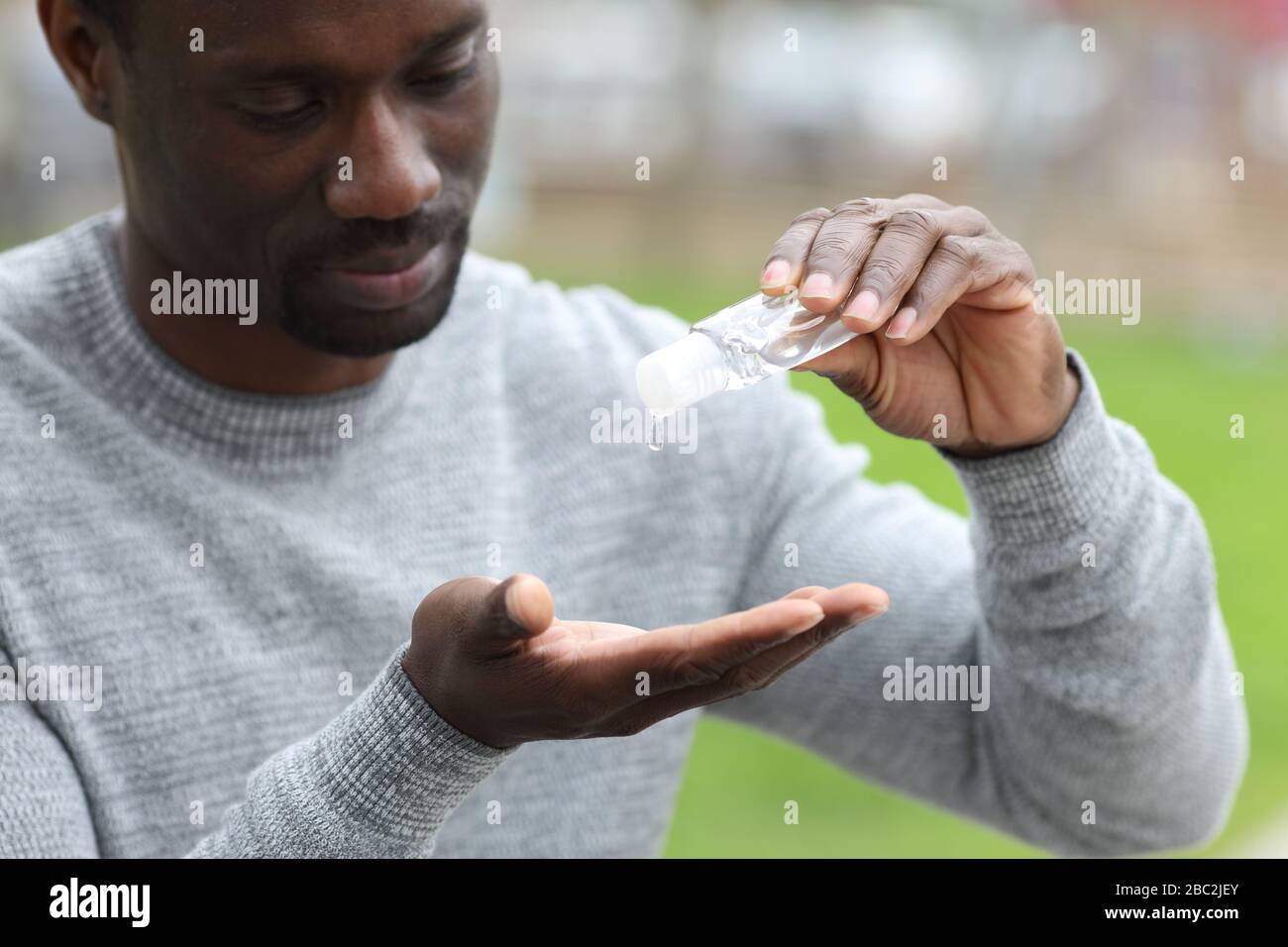 Uomo nero che pulisce le mani con sapone igienizzante all'aperto in un parco Foto Stock