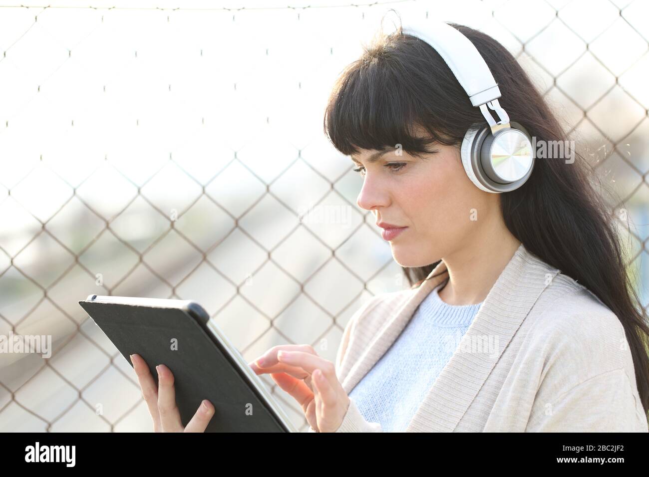 Donna adulta che impara a guardare i contenuti multimediali su tablet indossando cuffie in piedi per strada Foto Stock