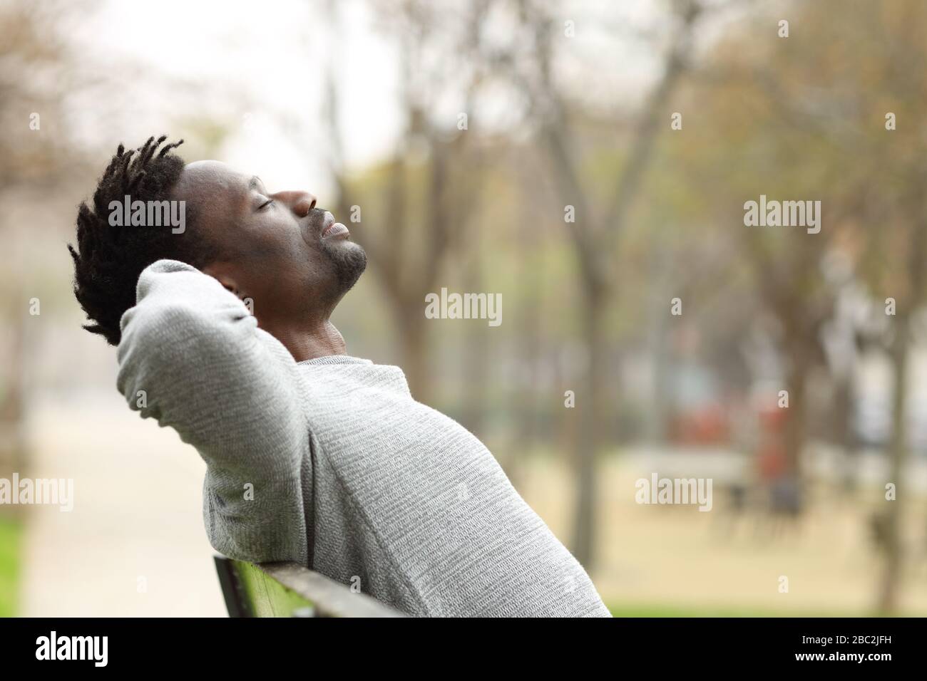 Vista laterale ritratto di un uomo nero rilassante seduta su una panchina in un parco Foto Stock
