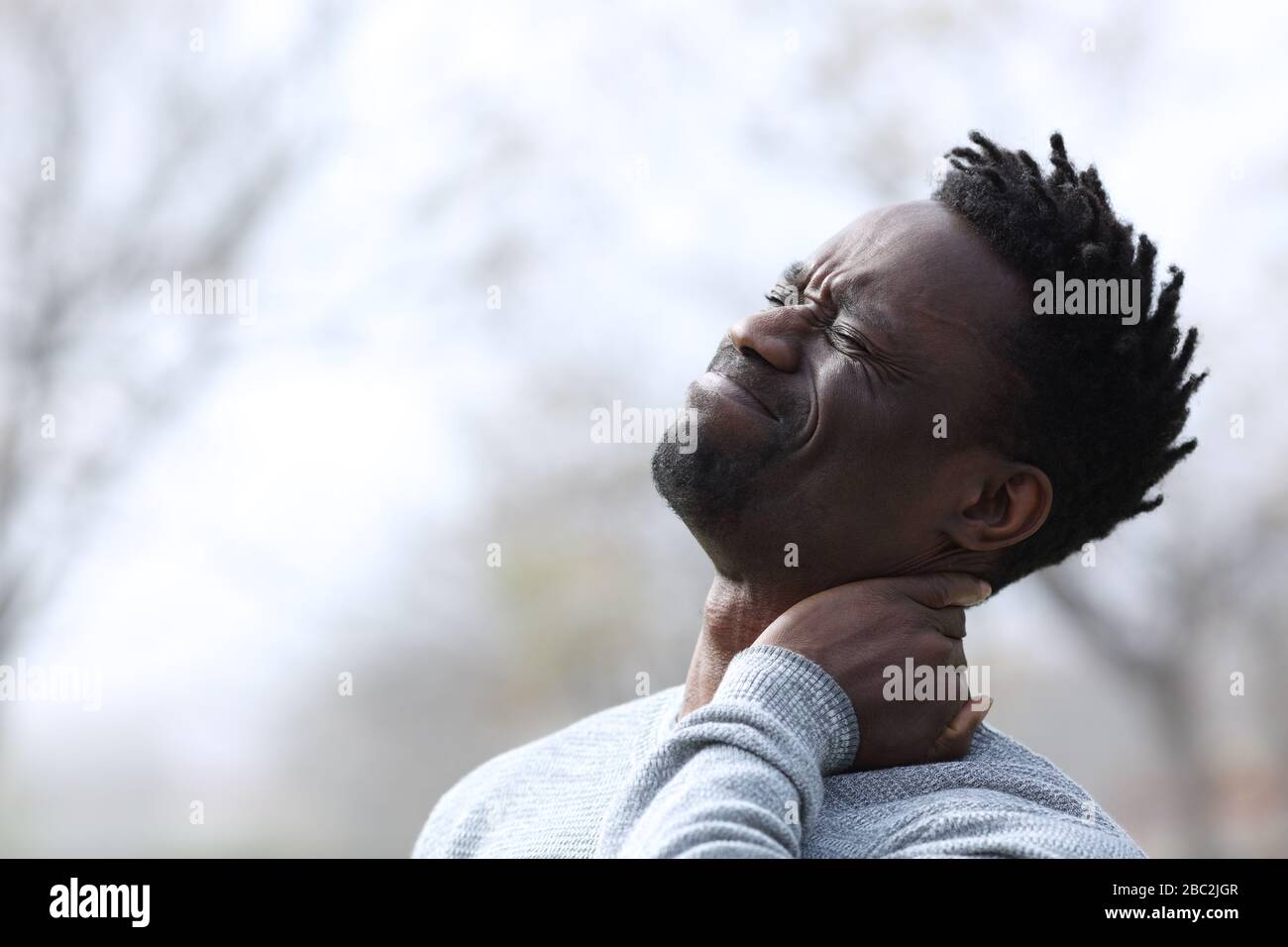 Uomo nero che soffre mal di collo lamentarsi all'aperto Foto Stock