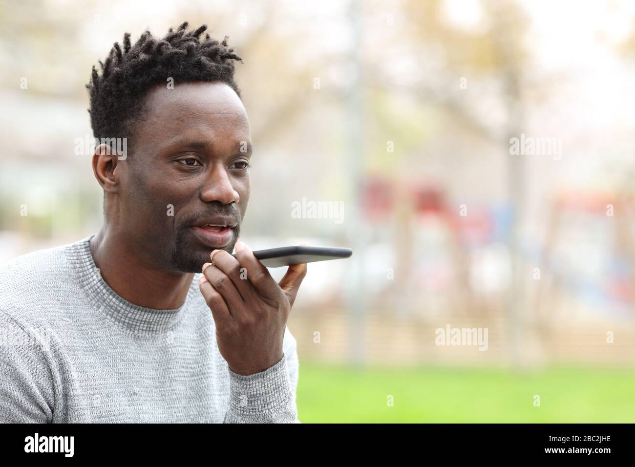 Ritratto di un uomo nero utilizzando il sistema di riconoscimento vocale sullo smartphone nel parco Foto Stock