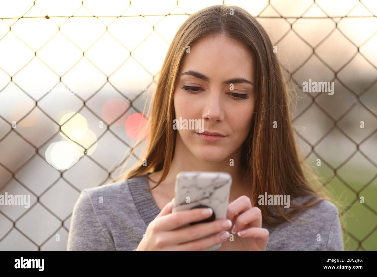 Vista frontale di una ragazza seria che usa lo smartphone in strada la sera Foto Stock