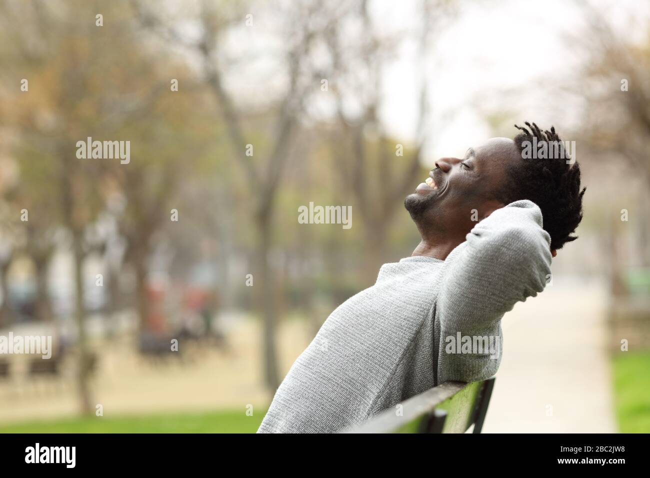 Vista laterale ritratto di un uomo felice nero rilassante seduto su una panchina in un parco Foto Stock