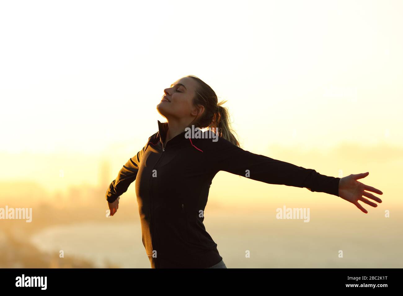Il corridore felice respira aria fresca che si allunga le braccia al tramonto nella periferia della città Foto Stock