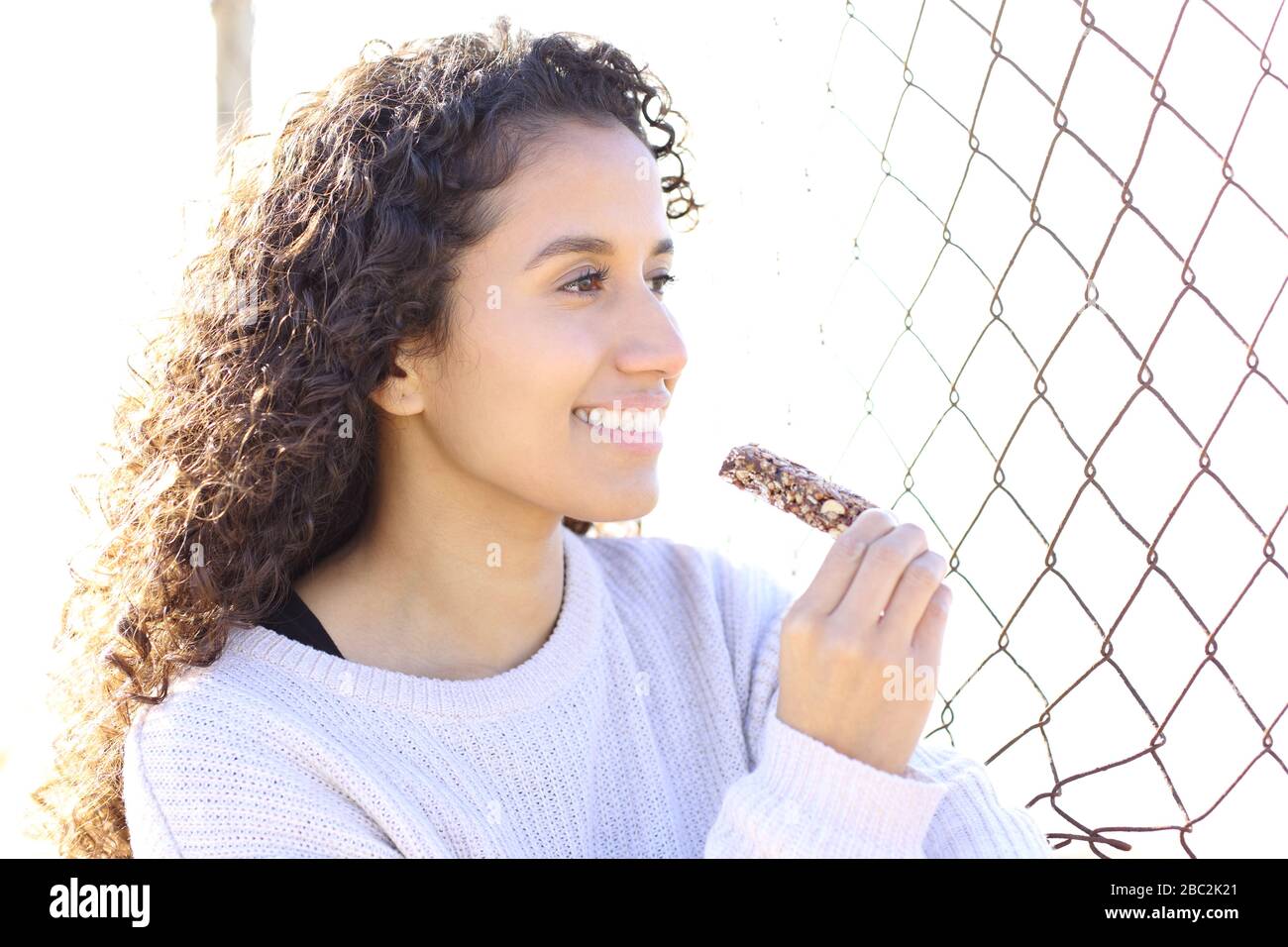 Ritratto di una giovane donna felice che mangia un cereale bar che guarda fuori Foto Stock