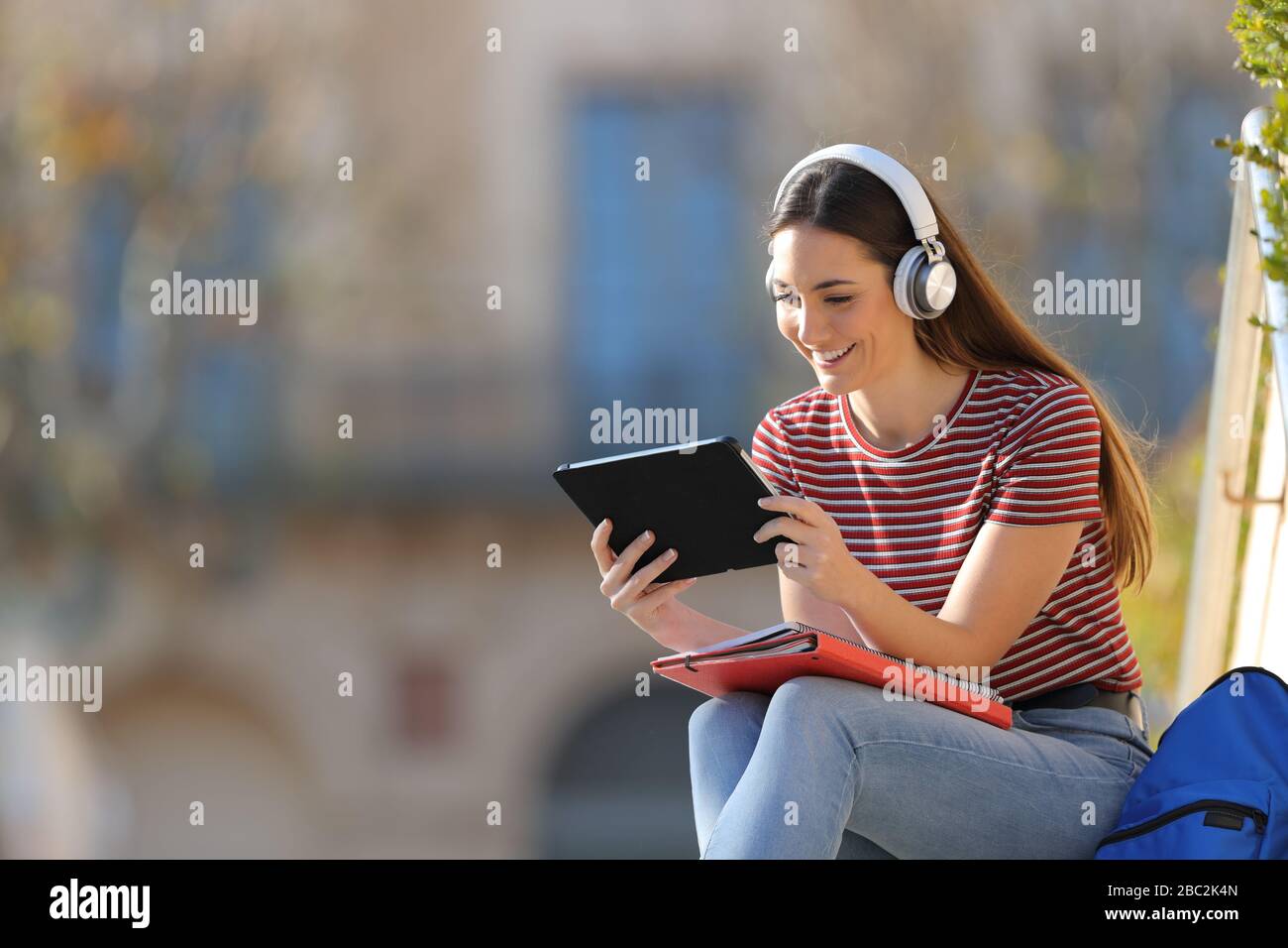 Buon studente con cuffie e tablet e imparare a stare seduti all'aperto in un campus universitario Foto Stock