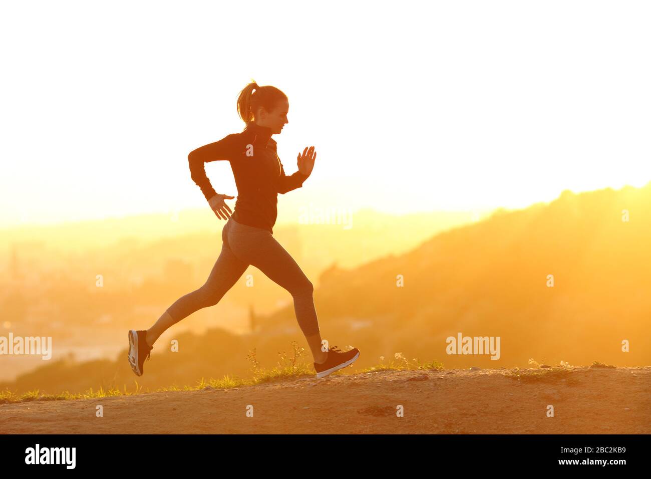 Profilo di una runner girl che corre al tramonto in montagna con una calda luce arancione Foto Stock