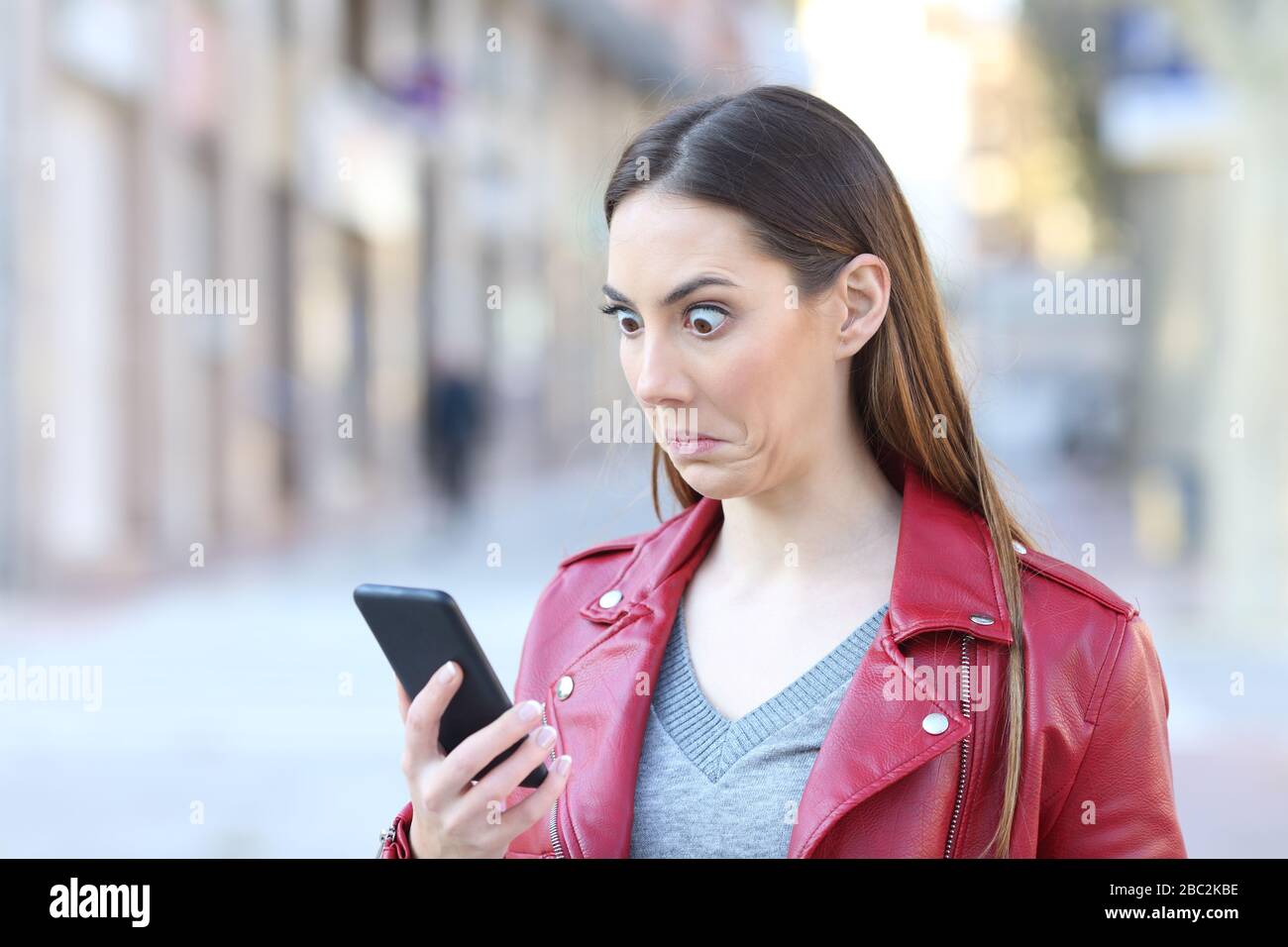 Perplessa donna che controlla le notizie del telefono intelligente in piedi nella strada Foto Stock
