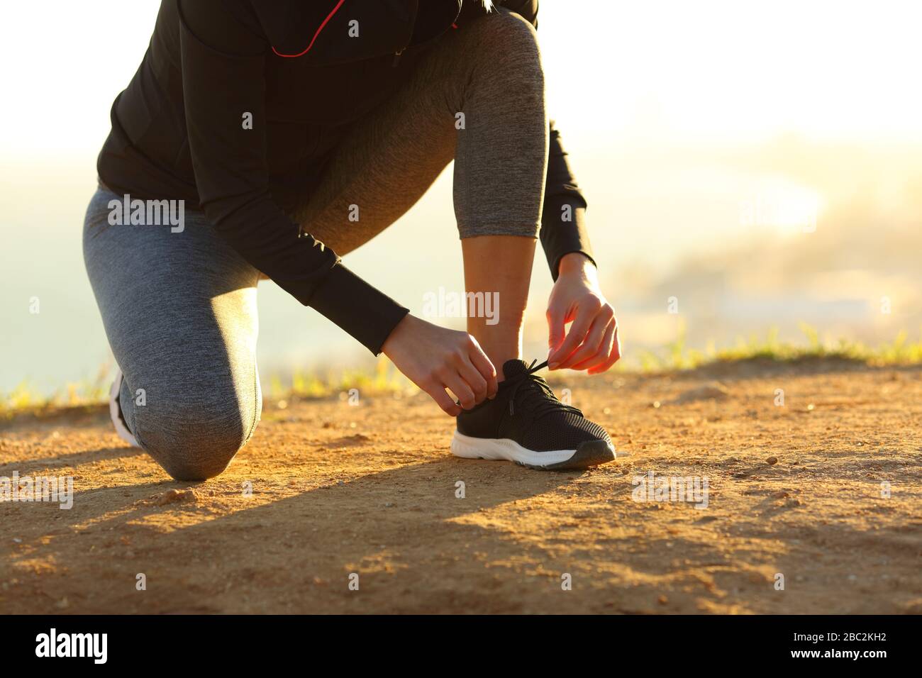 Runner donna mani legando scarpe di scarpe a terra al tramonto Foto Stock