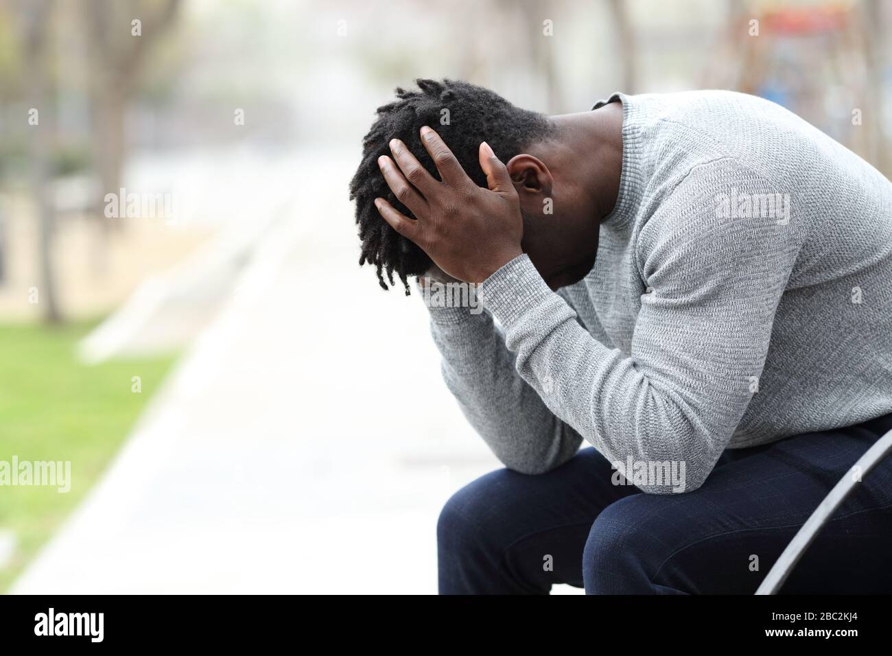 Vista laterale ritratto di un triste uomo nero depresso seduto su una panchina in un parco Foto Stock