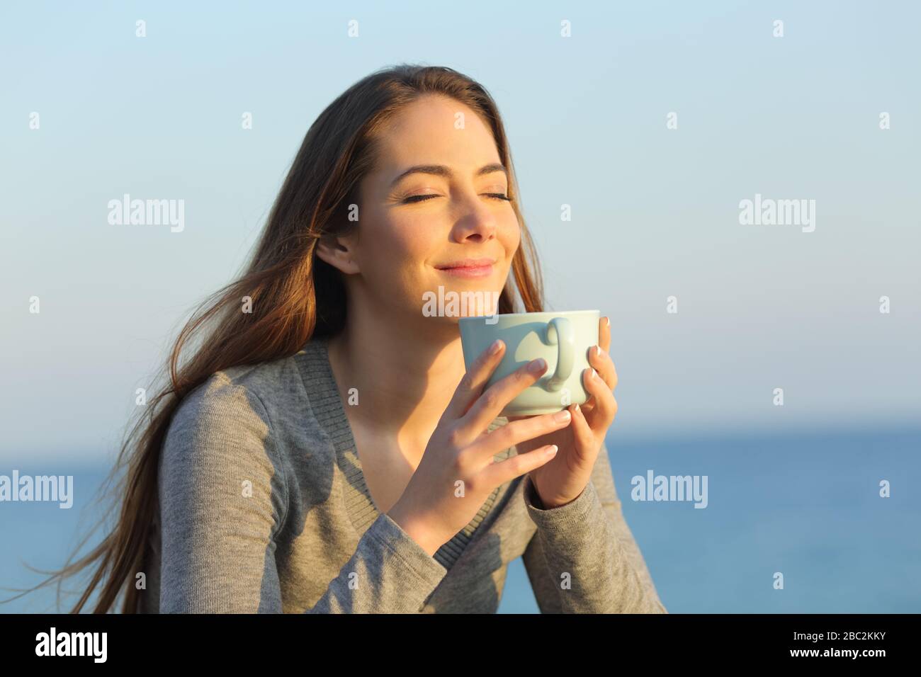 Donna soddisfatta con occhi chiusi bere caffè al tramonto sulla spiaggia Foto Stock