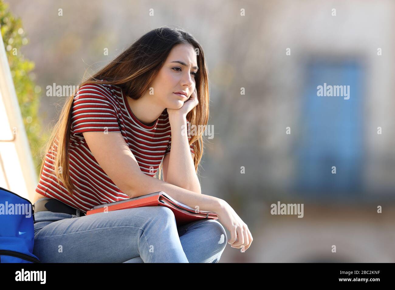 Triste studente lamentarsi guardando lontano seduto in un campus Foto Stock