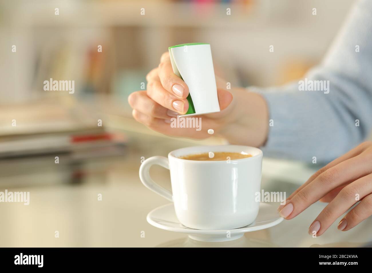 Primo piano di donna mano che getta saccharina pillole su tazza di caffè su una scrivania a casa Foto Stock