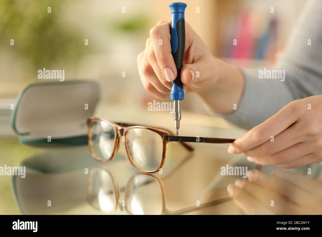 Primo piano delle mani della donna avvitare gli occhiali con un cacciavite su una scrivania a casa Foto Stock