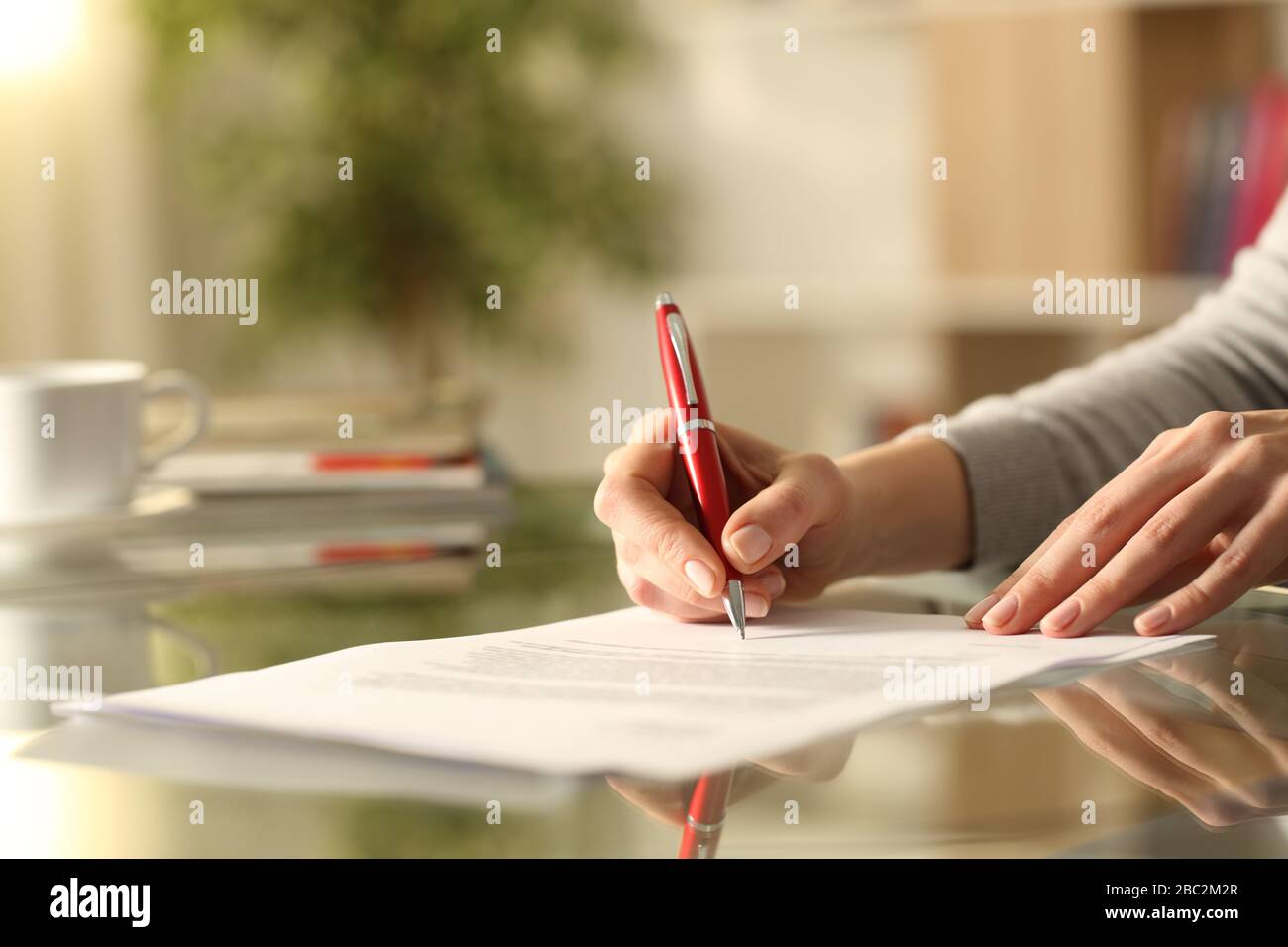 Primo piano di donne mani firma documento con penna su una scrivania a casa Foto Stock