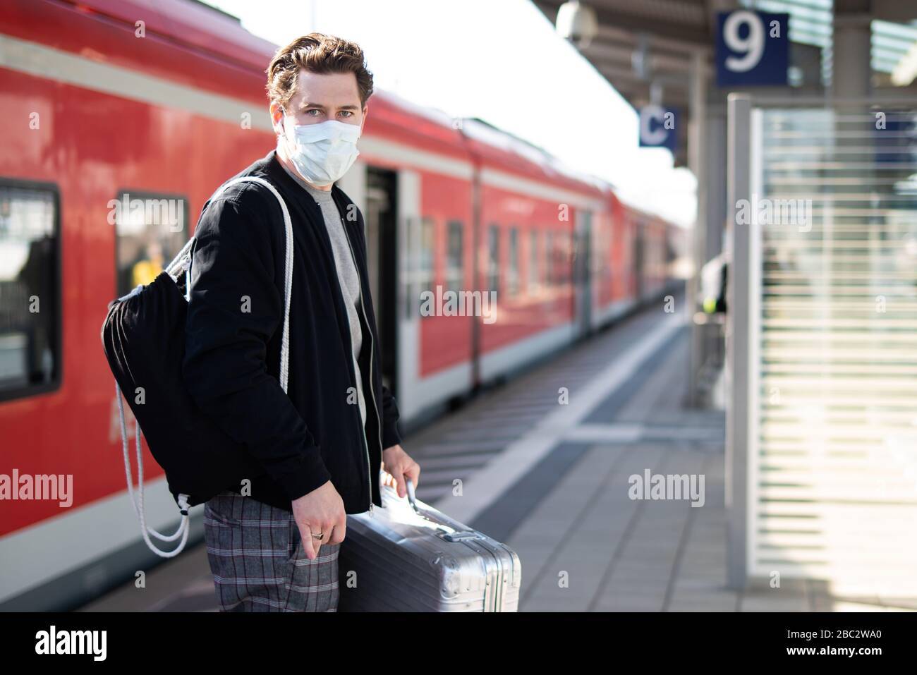 Uomo con una valigia sulla piattaforma, ha una maschera facciale e guanti contro l'infezione con il virus corona Foto Stock