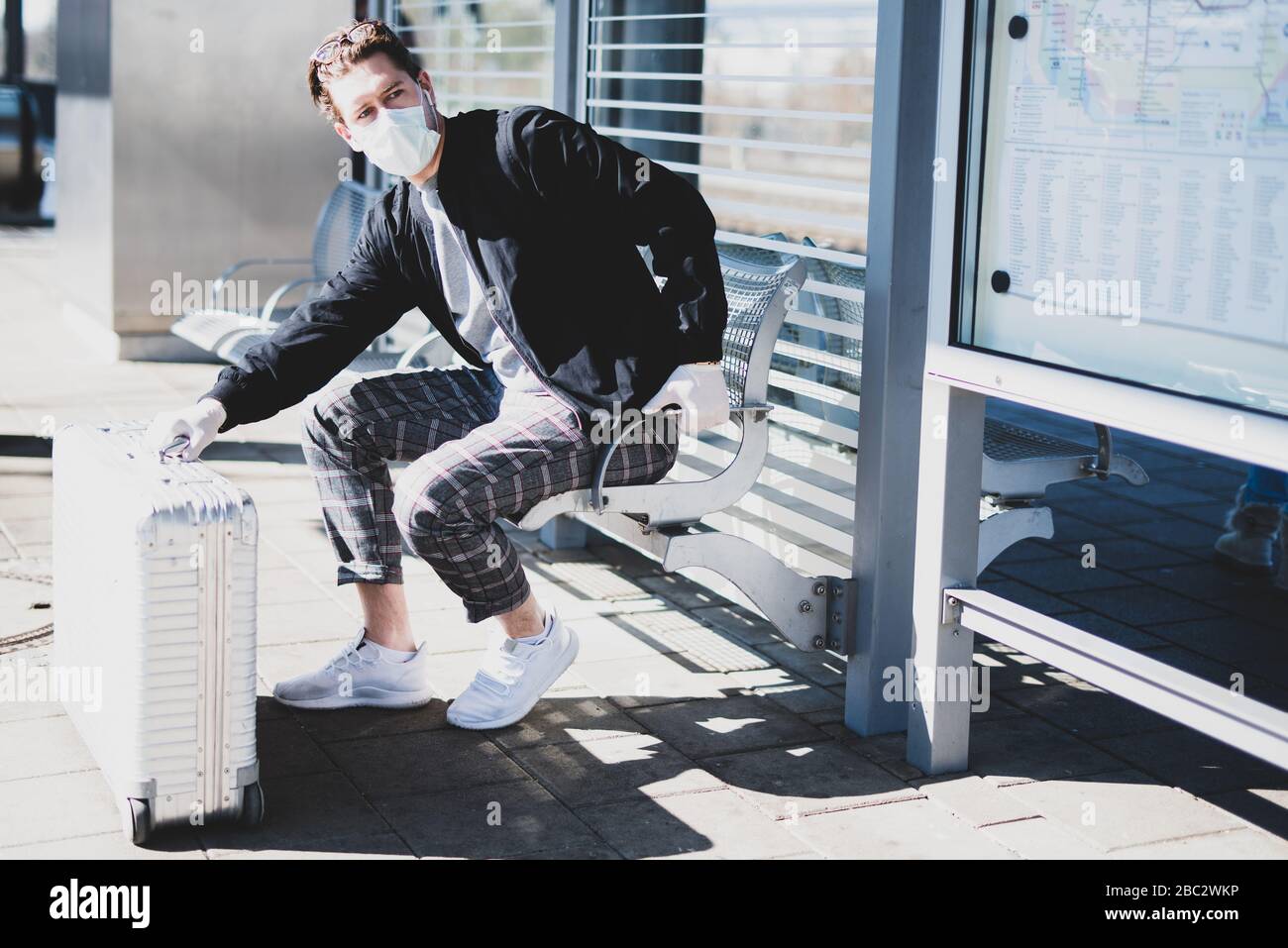 Un uomo sta aspettando un treno sulla piattaforma, indossando una maschera facciale e guanti di gomma per proteggersi dal virus corona Foto Stock