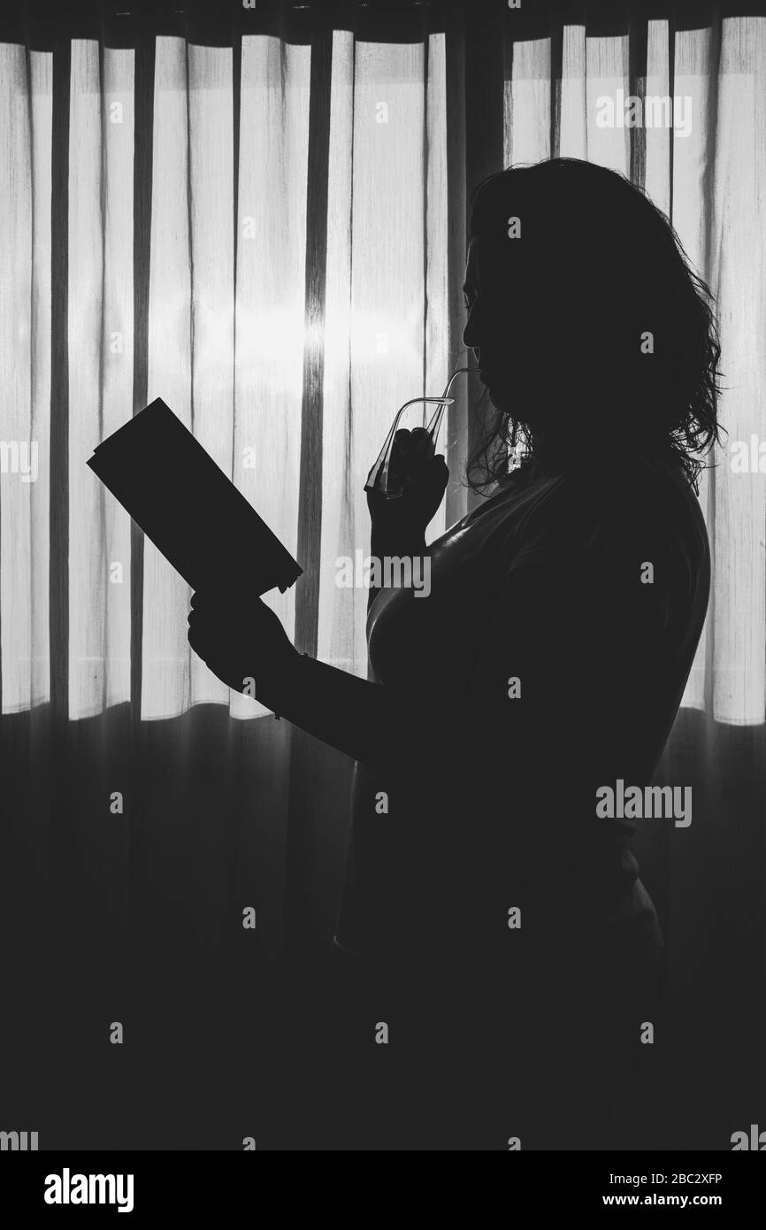 Vista laterale della silhouette donna in piedi accanto alla finestra leggendo un libro Foto Stock