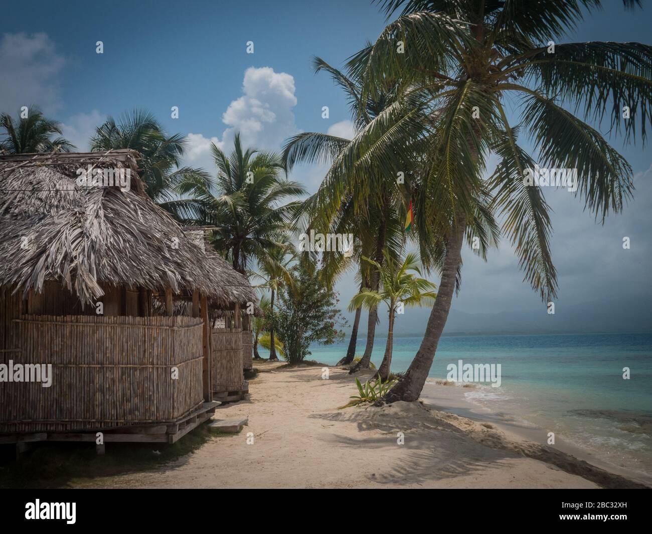 Capanne d'erba dietro una fila di palme che si trovano sul bordo del cristallino, acquamarina, oceano caraibico su un'isola al largo di Panama. Foto Stock