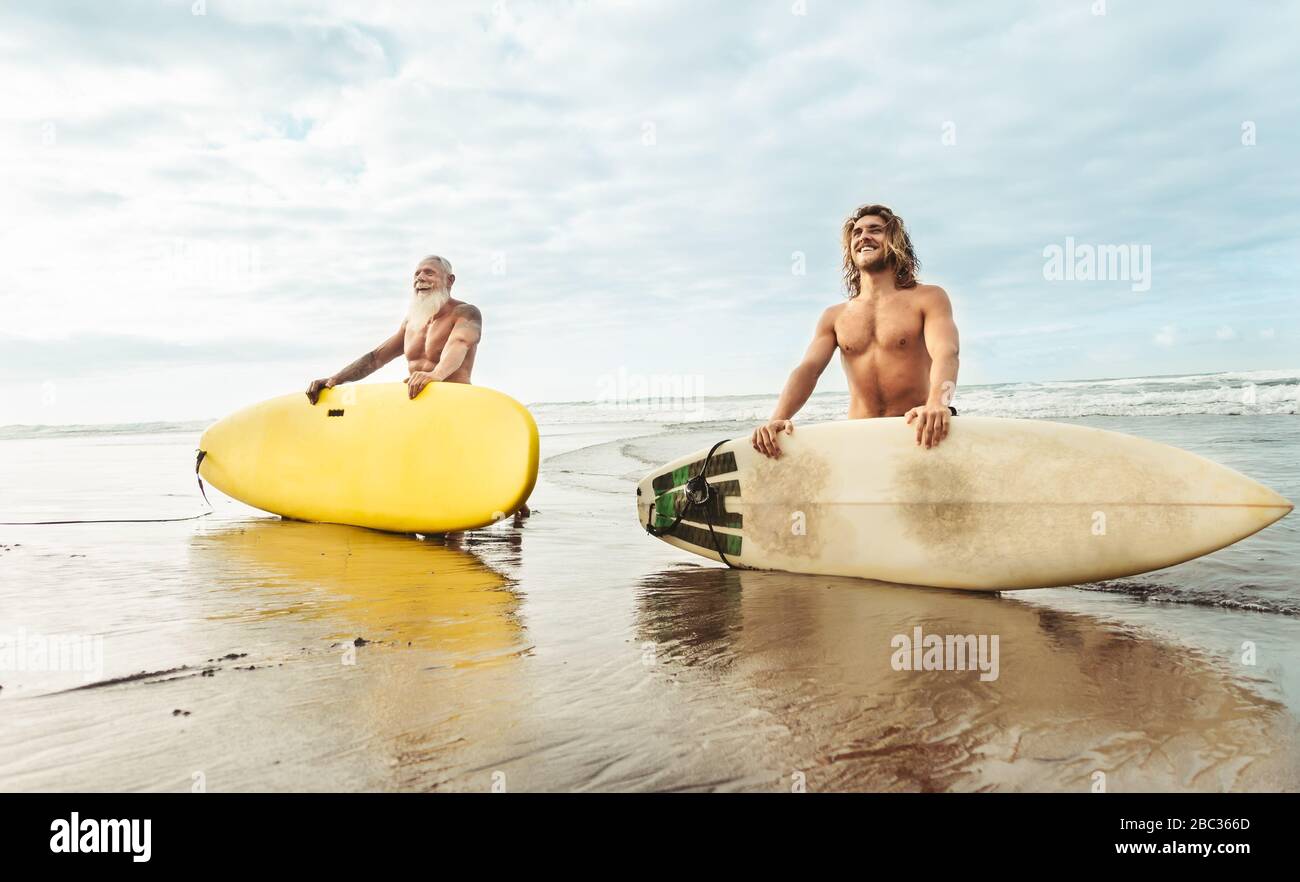 Montare felici amici divertendosi surf sul oceano tropicale - Surfers padre e figlio facendo stretching esercizi di surf Foto Stock