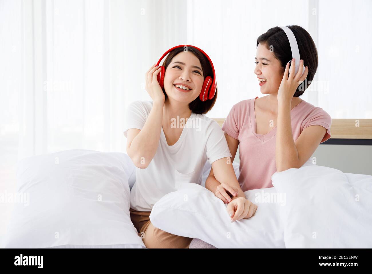 Due donne asiatiche felici indossano le cuffie e godono di musica o canzoni che gradiscono nella camera da letto. Foto Stock