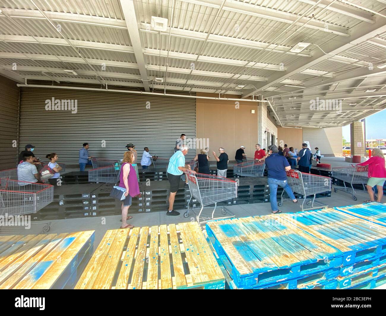 Gli acquirenti si allineano a Costco mantenendo le distanze sociali. Palette di legno sono state messe per aiutare la gente a tenere a parte e forma una linea con abbastanza spazio tra di loro. Foto Stock