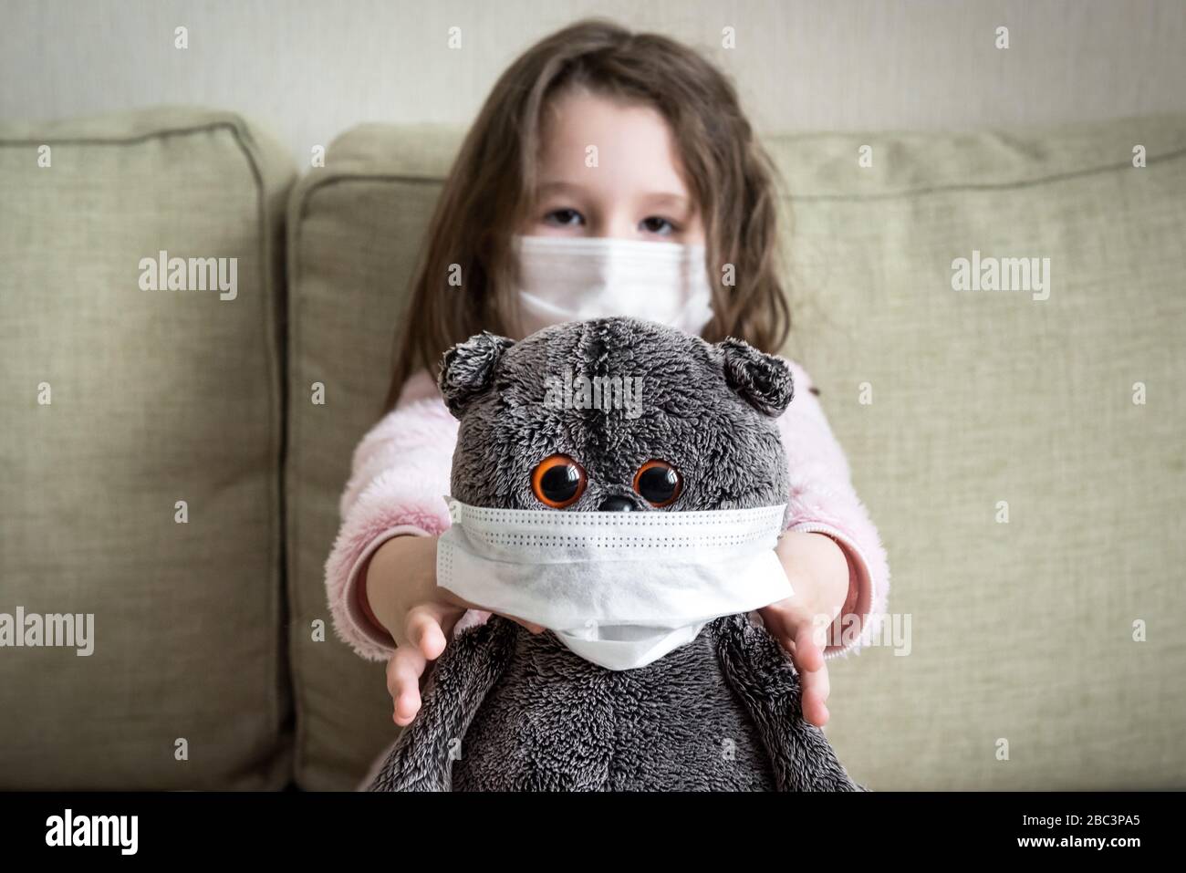 Concetto di quarantena per coronavirus, la bambina gioca con il giocattolo a casa durante la pandemia di COVID-19. Capretto in maschera medica per la protezione al virus corona indoor Foto Stock